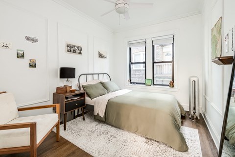 a bedroom with a bed and a desk and two windows
