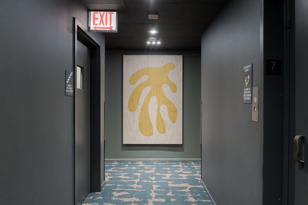 a hallway with an exit sign and a painting on the wall in a hotel room