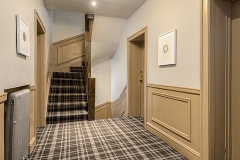 A hallway with a staircase and a wall-mounted clock.
