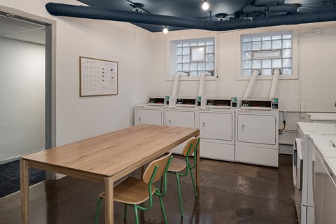 A kitchen with a table and chairs in the foreground and a calendar on the wall.