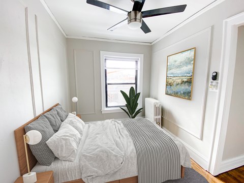 A bedroom with a bed, a ceiling fan, and a painting on the wall.