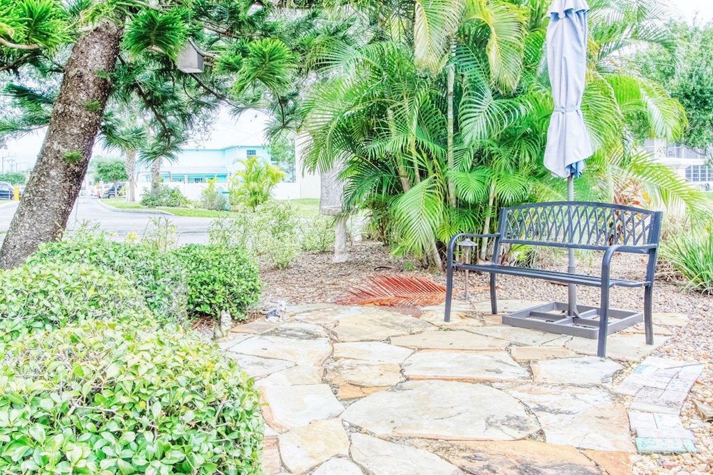 outside patio with metal bench and umbrella surrounded by lush landscaping