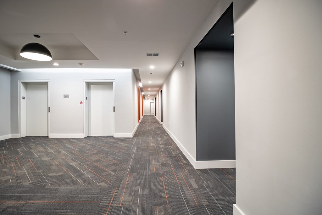 a corridor with white walls and grey flooring and a hallway with white and black