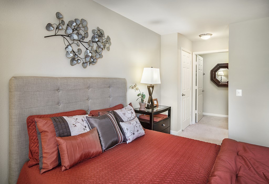 a bedroom with a bed with red pillows and a grey headboard