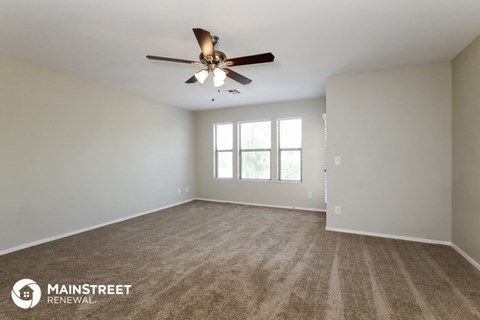 the spacious living room with ceiling fan and carpeting