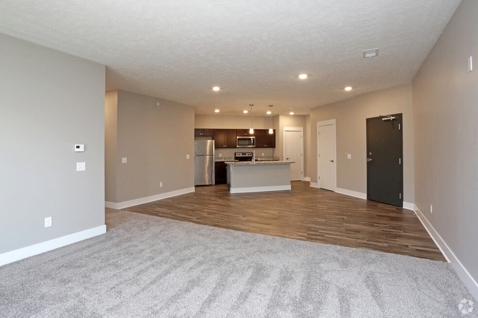 an empty living room with a kitchen in the background