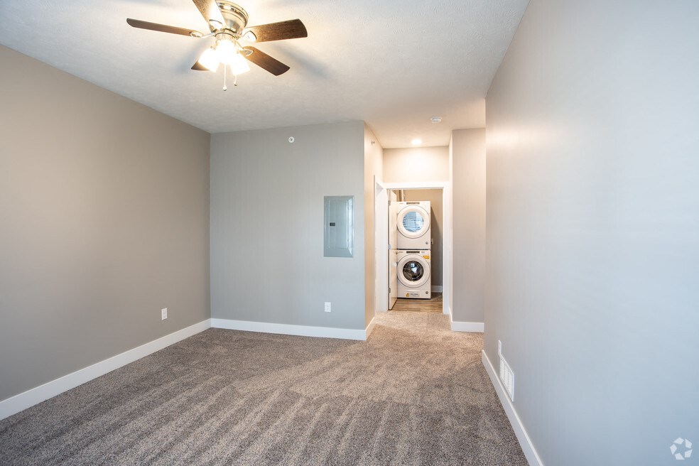 an empty living room with a ceiling fan and a laundry room