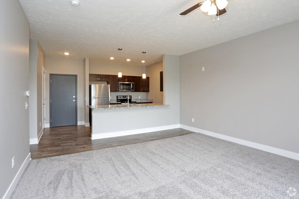 an empty living room with a kitchen and a ceiling fan