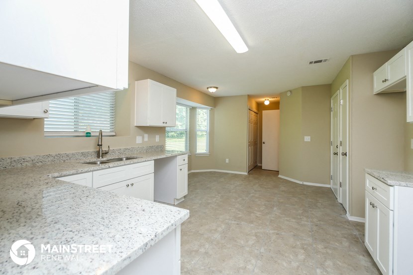 a large kitchen with white cabinets and granite counter tops and a door to a hallway