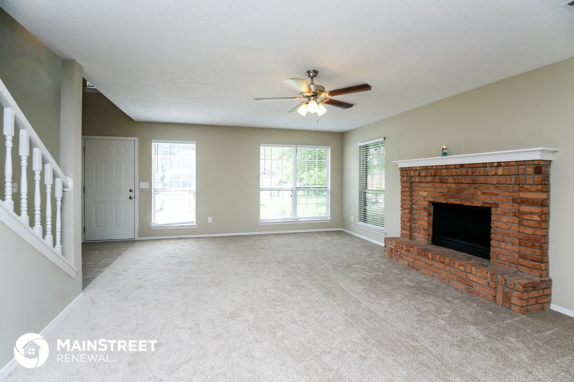 an empty living room with a brick fireplace and a ceiling fan