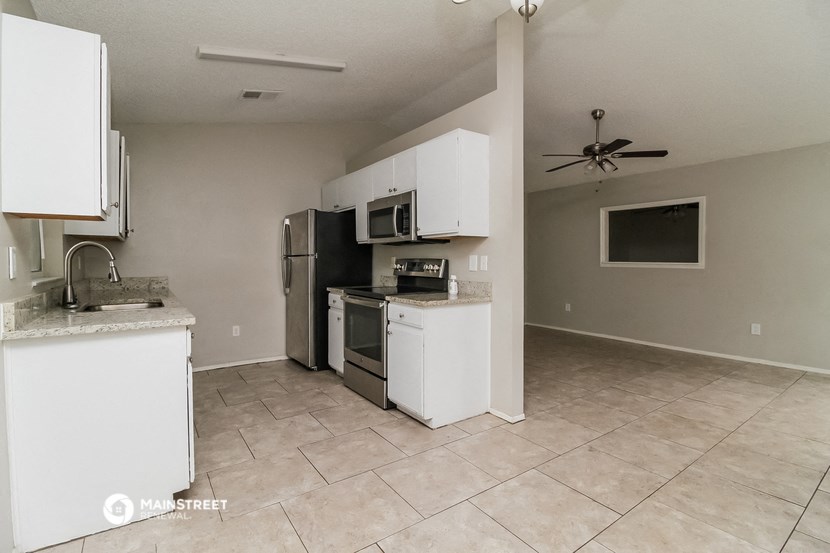 an empty kitchen with white cabinets and appliances and a ceiling fan