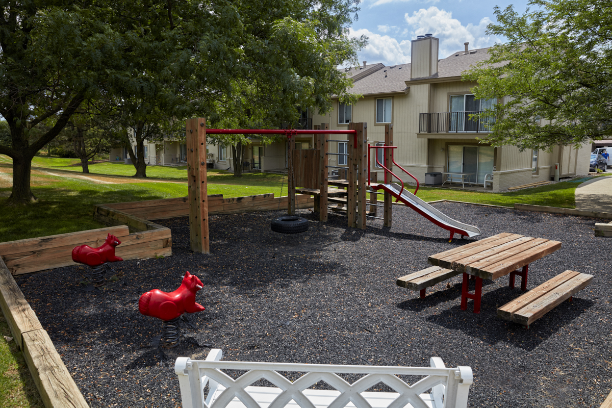 a playground with a swing set and benches in front of an apartment building