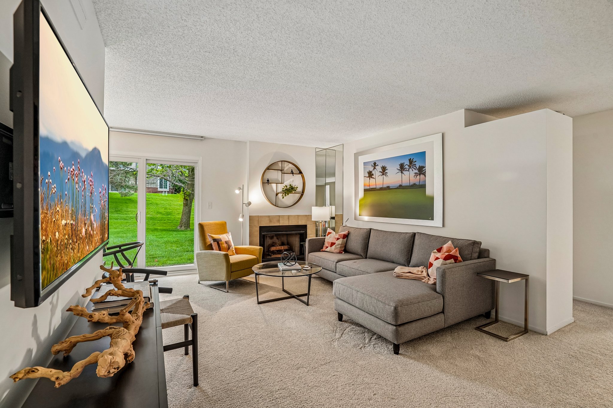 A living room with a grey couch, a yellow chair, and a painting of a landscape on the wall.