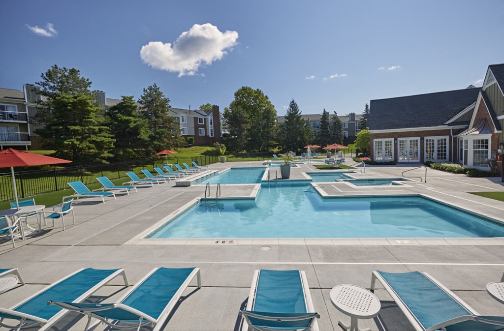 a swimming pool with blue chairs and umbrellas in front of a house