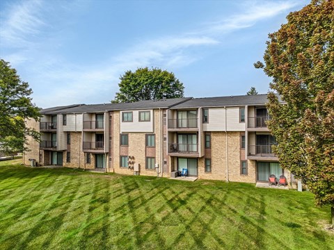 an apartment building with a green lawn and trees