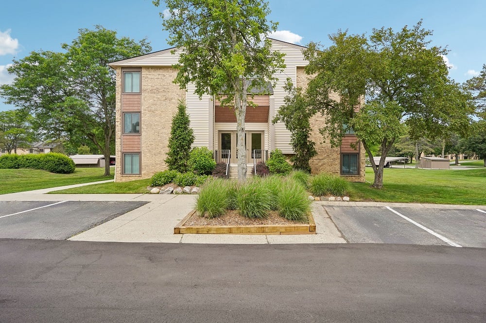 A building with a front yard and a parking lot in front.