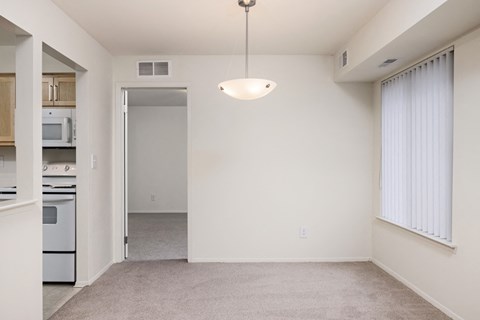 the living room and kitchen of an apartment with white walls and carpeting