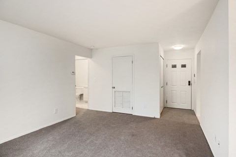 a living room with white walls and carpet and a door to a bathroom