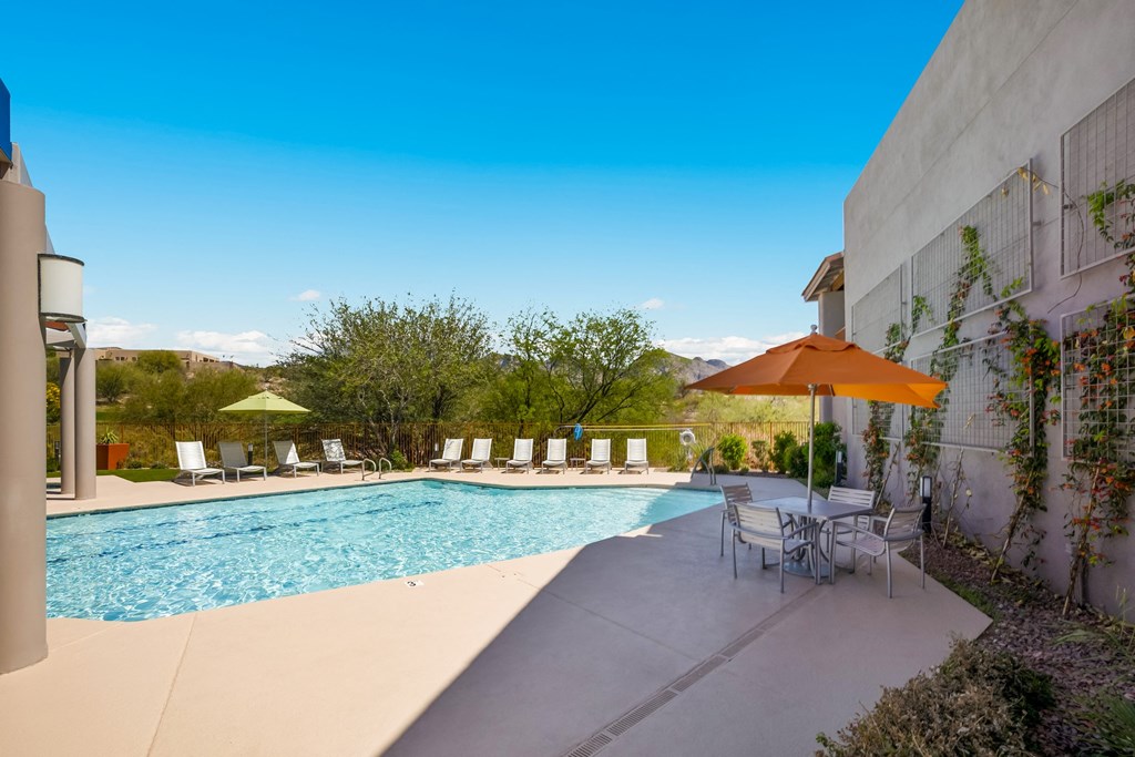 the pool is next to a patio with chairs and an umbrella