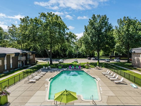a swimming pool with lounge chairs and umbrellas in a yard with trees