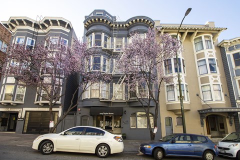 A row of three-story buildings with a car parked in front of them.