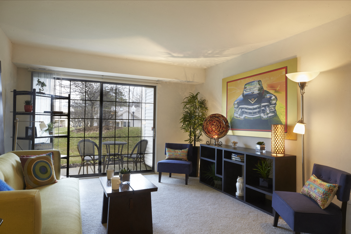 A living room with a yellow couch, a blue couch, a wooden coffee table, a side table with a lamp, a potted plant, and a painting on the wall.