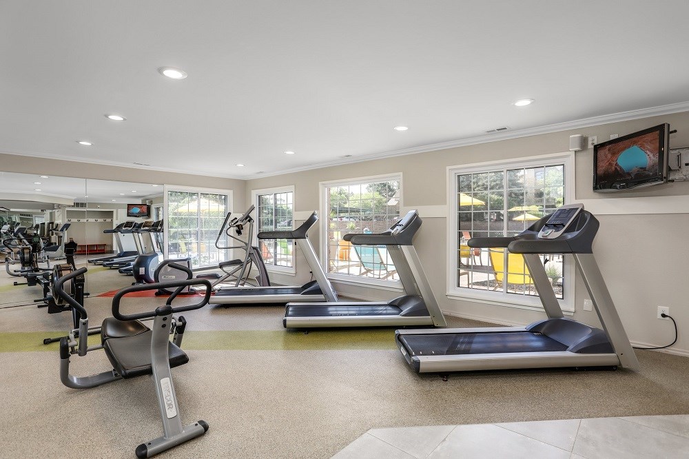 a gym with treadmills and other exercise equipment in a room with windows