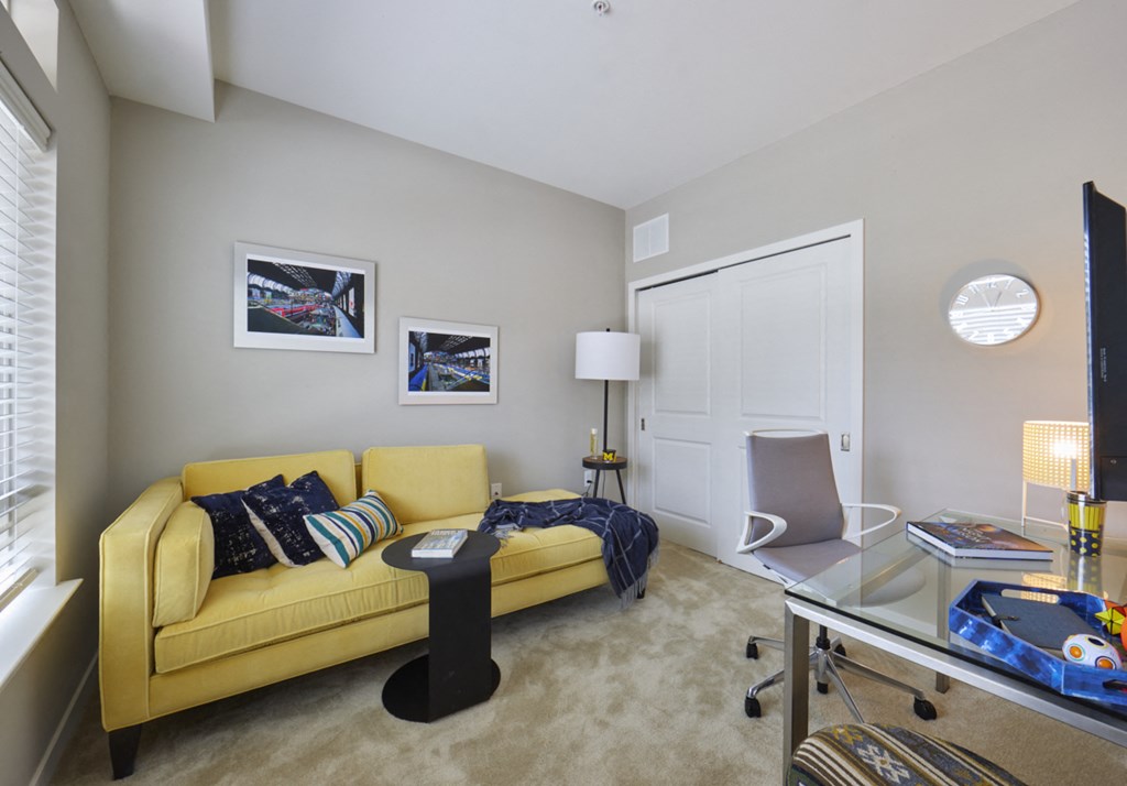 a living room with a yellow couch and a glass desk