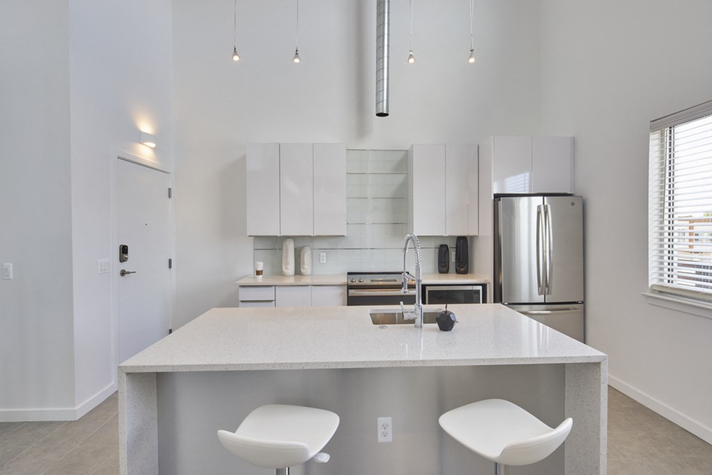 a kitchen with white cabinets and a large island with two white chairs