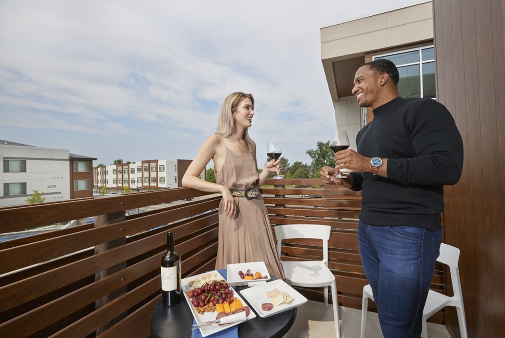 a man and a woman standing on a balcony with wine and food