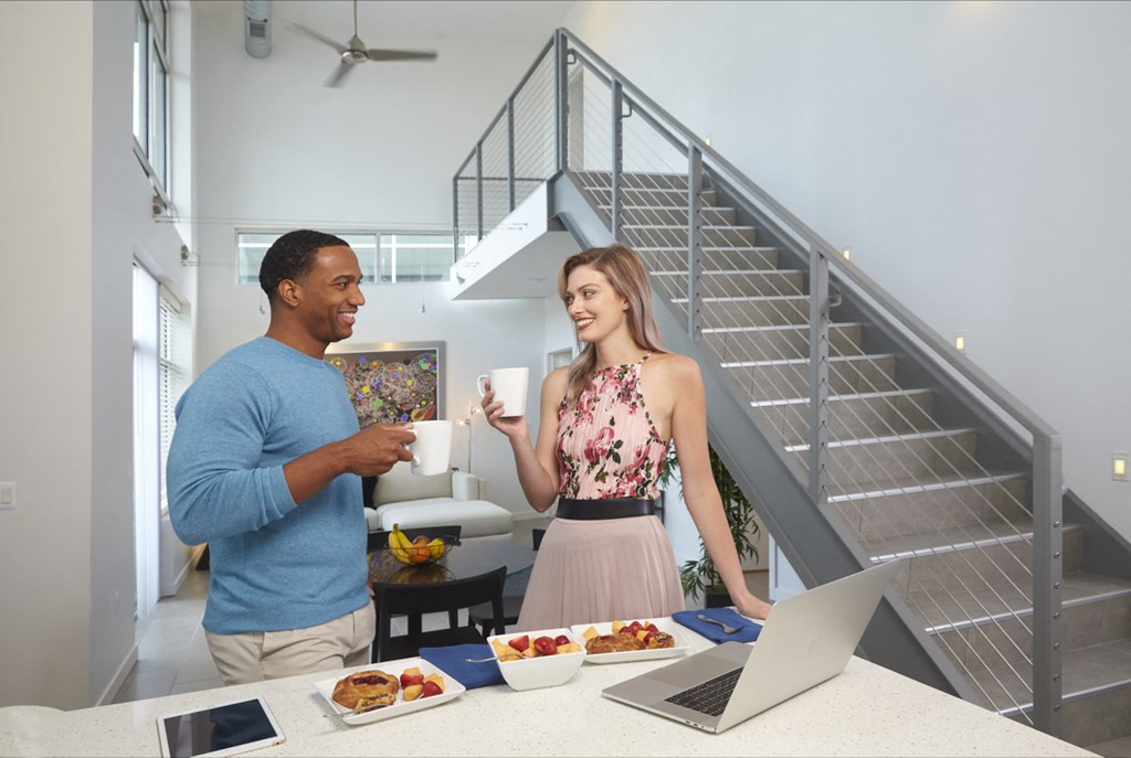 a man and a woman standing at a table with food and a laptop