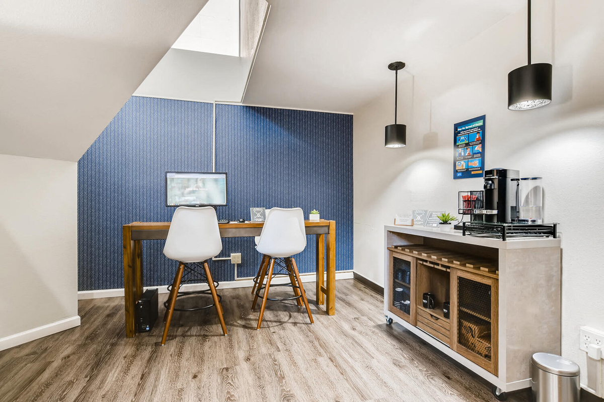 a dining room with a table and two chairs and a kitchen with a coffee machine