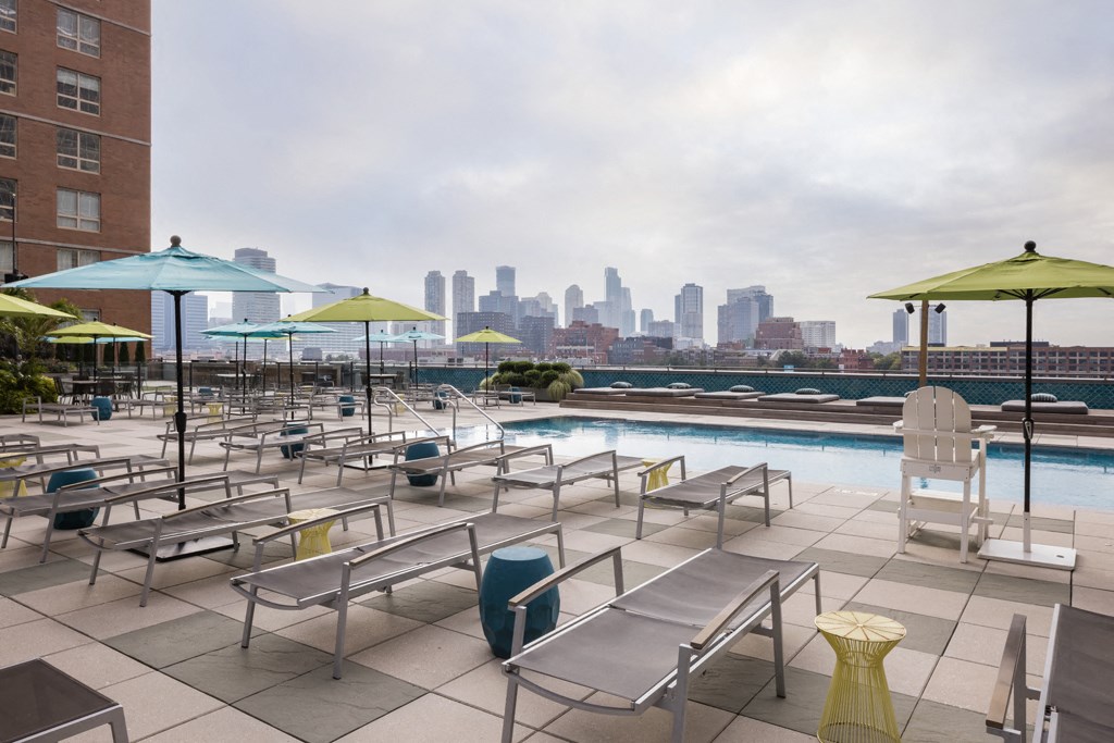 a pool with chairs and umbrellas and a city skyline in the background