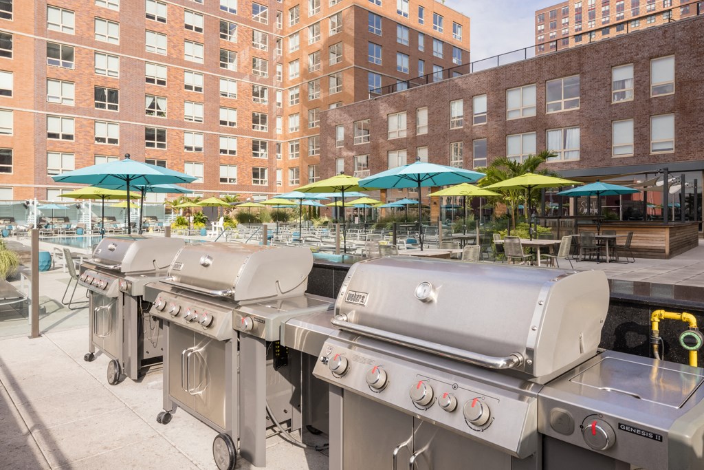 three stainless steel bbq grills in front of umbrellas and tables