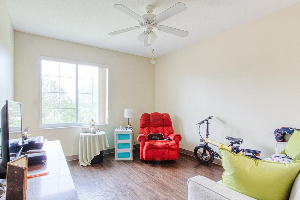a living room with a red chair and a ceiling fan