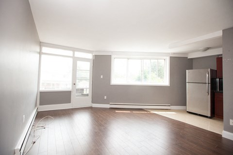 an empty living room with a refrigerator and a window