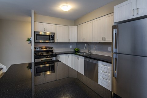 A kitchen with a black counter top and stainless steel appliances.