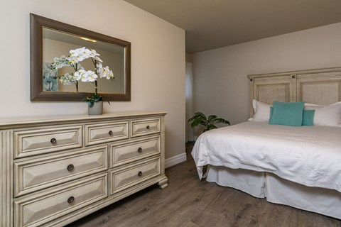 A bedroom with a bed, dresser, and a mirror with a flower arrangement on top.