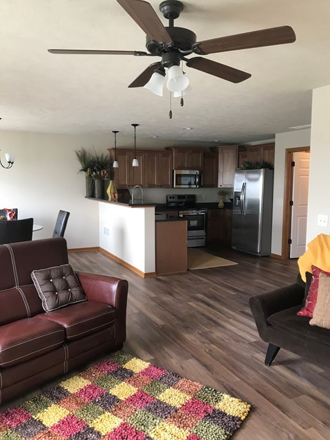 A brown leather couch sits in a kitchen with a ceiling fan.