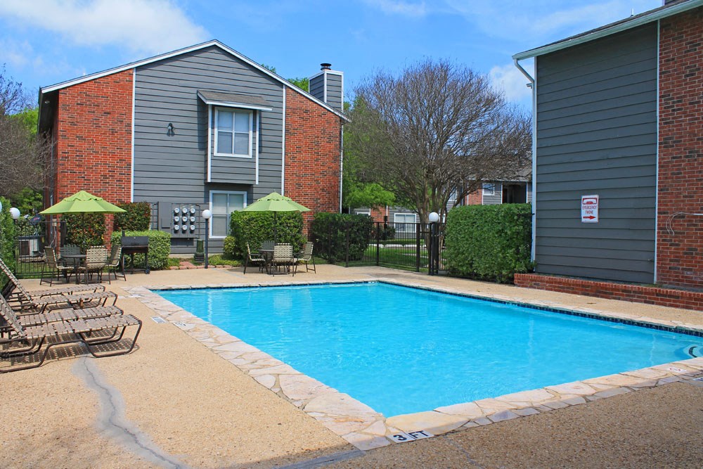 a swimming pool with chairs and umbrellas in front of a house