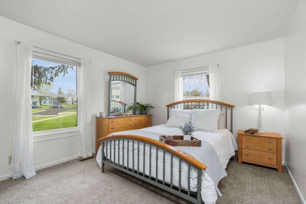 A bedroom with a large bed, a window with a view of a street, and a nightstand with a lamp.
