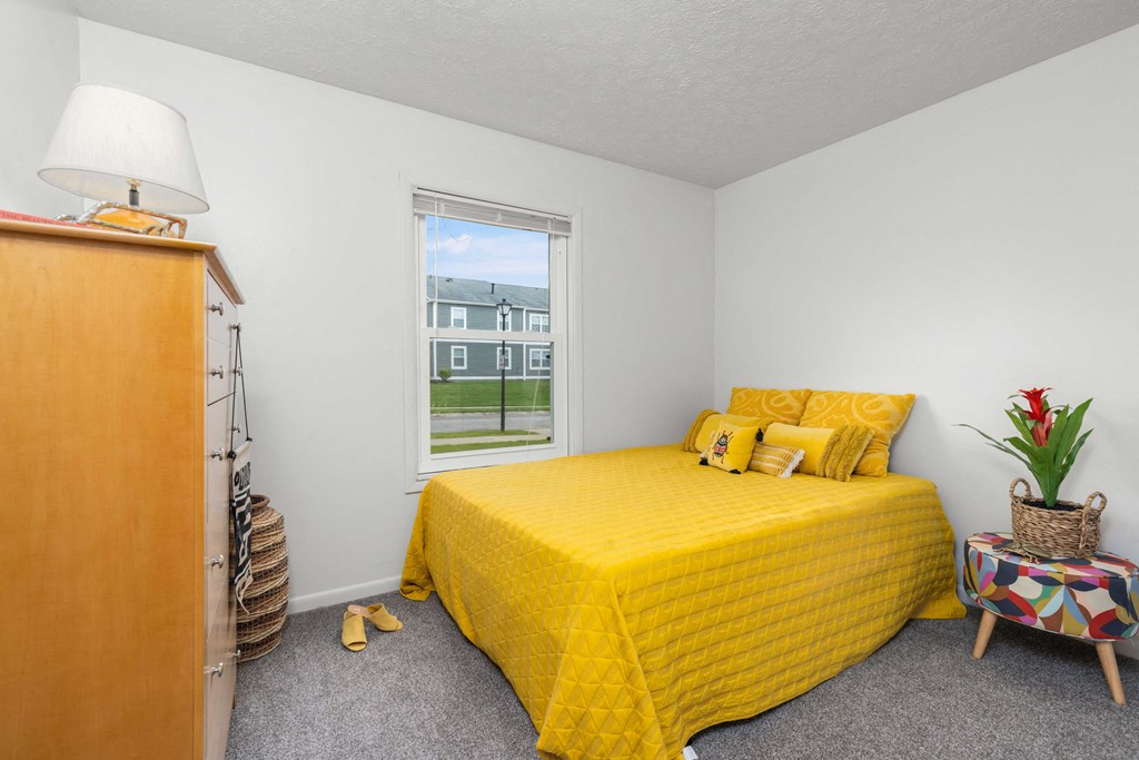 A bedroom with a yellow bedspread and a window showing a view of a building.