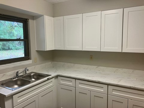 A kitchen with white cabinets and marble countertops.