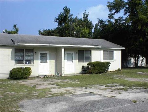A white house with a grey roof and a small front yard.