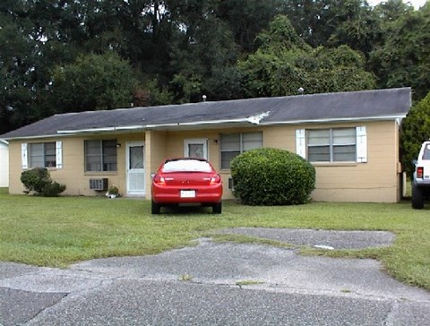A red car is parked in front of a beige house.