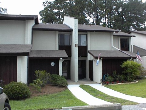 A white house with a brown roof and a car parked in front.