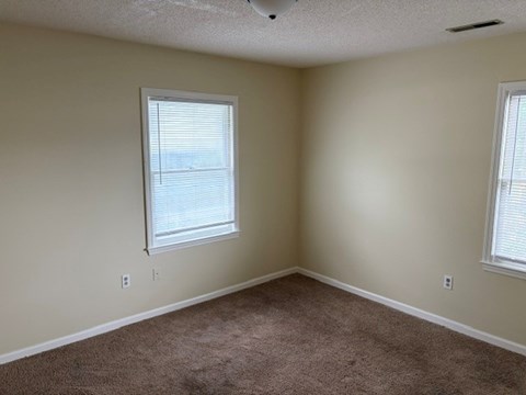 A room with a carpeted floor and two windows.