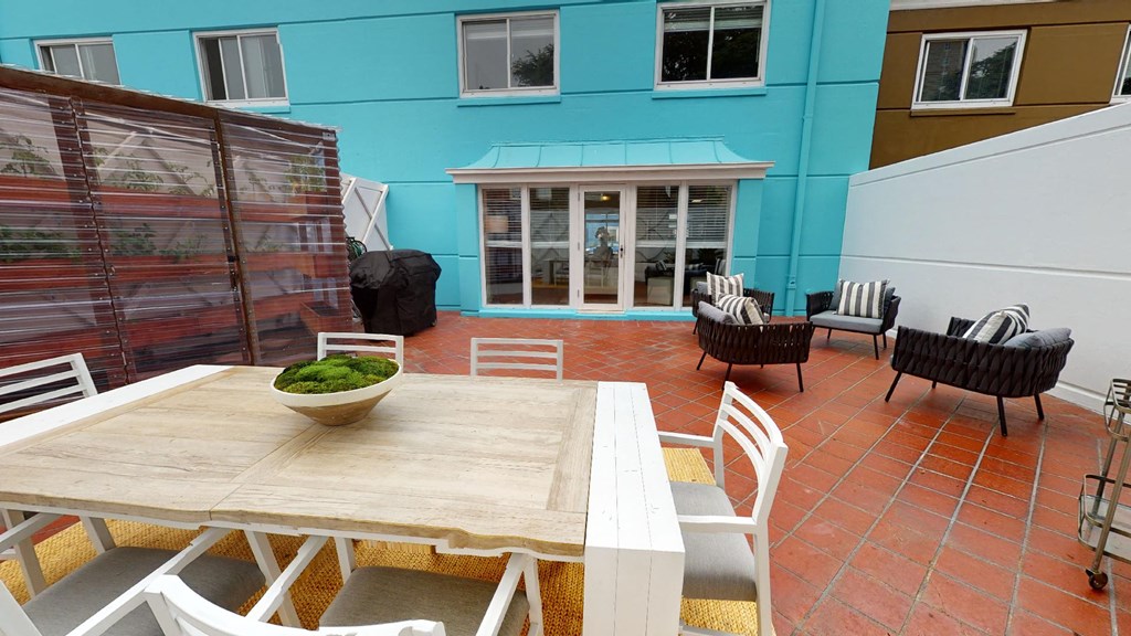 a patio with a wooden table and chairs in front of a blue building
