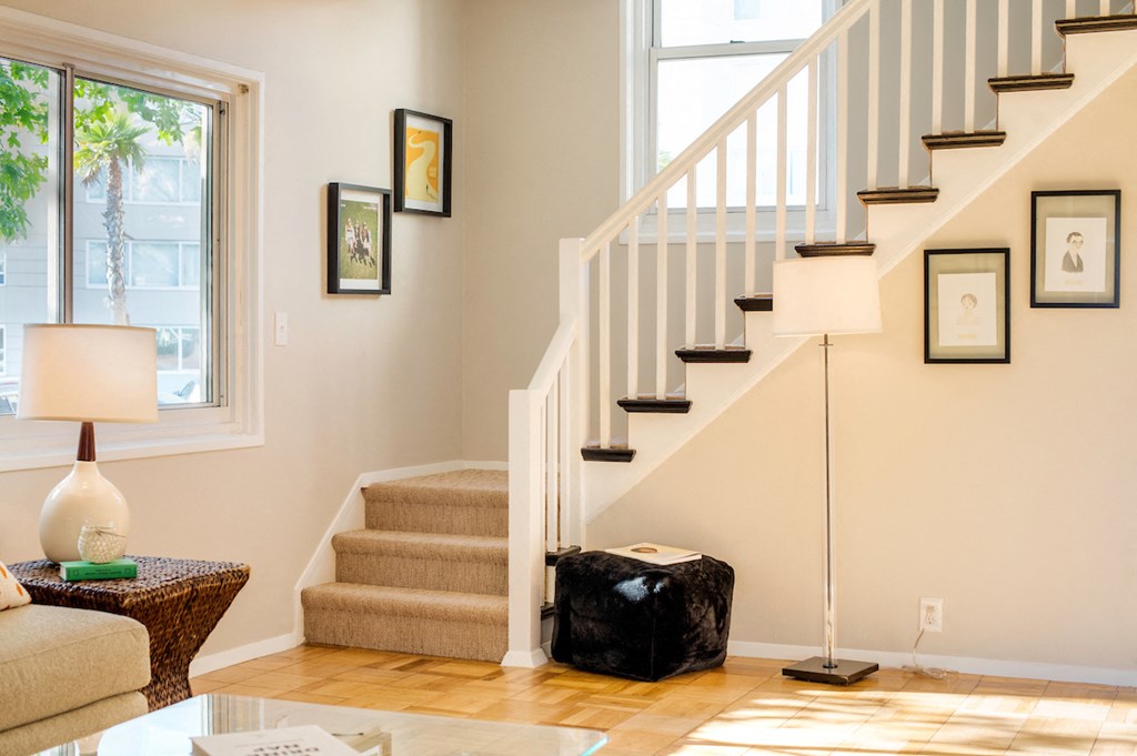 a staircase in a living room with a black ottoman next to a window
