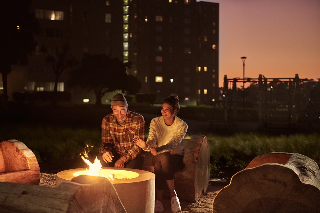 a man and woman sitting around a fire pit at night
